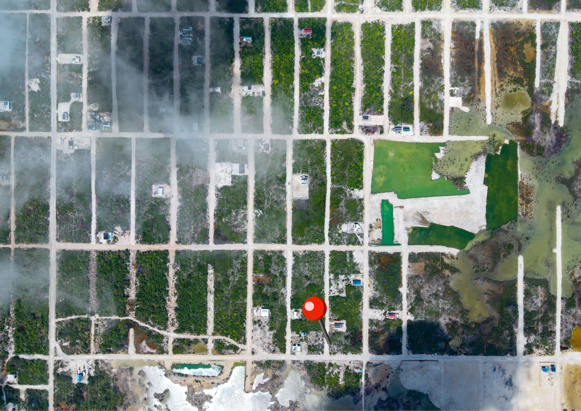 Aerial view of a grid of vacant lots with scattered small buildings and a red location pin