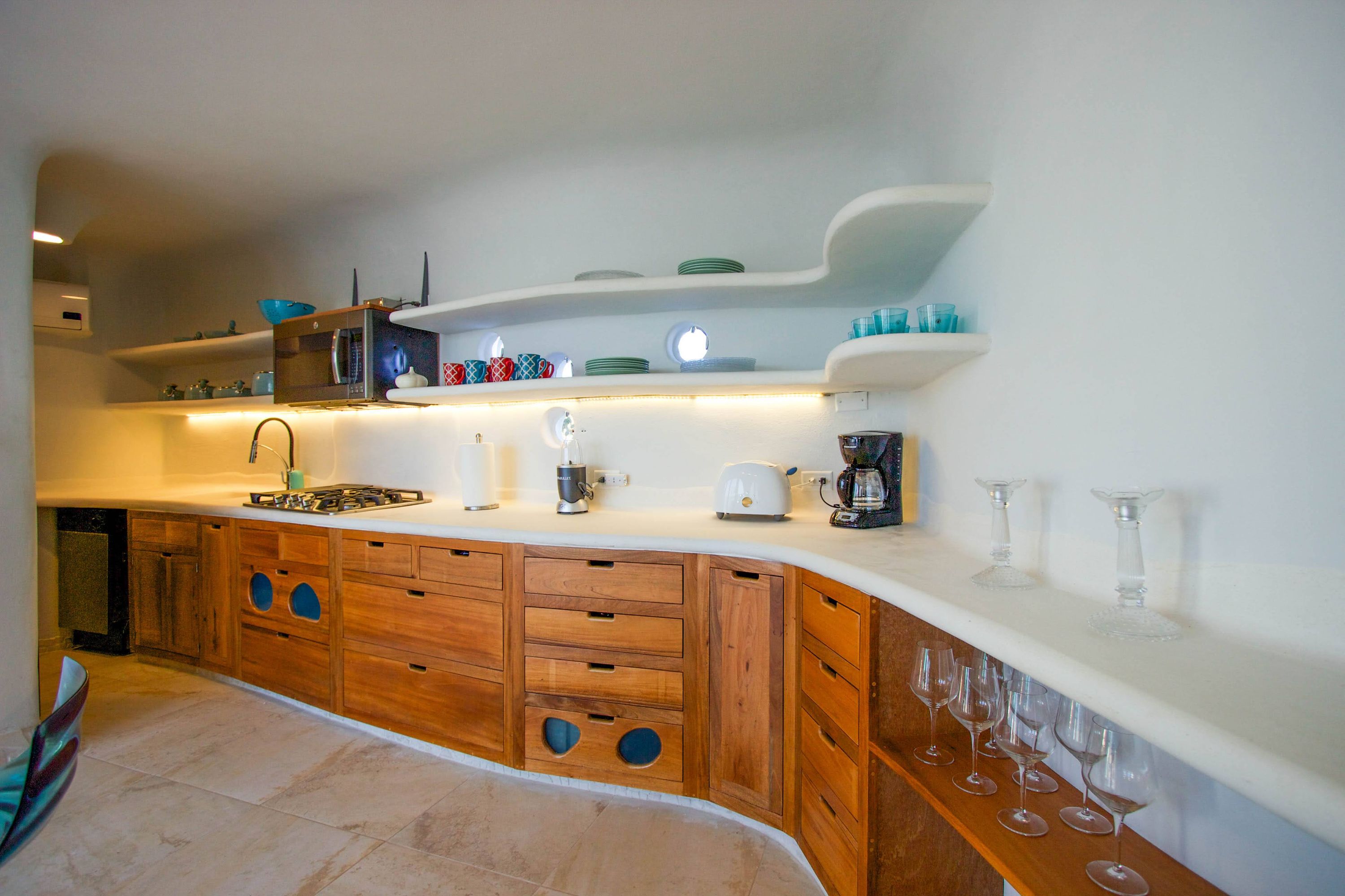 Kitchen counter with wood cabinets, white toaster and blender beneath curved shelves