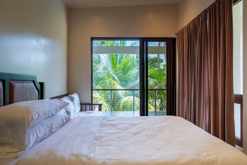 Bedroom with glass doors opening to balcony and palm trees beyond