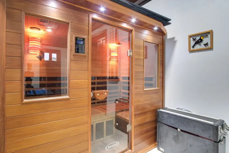 Wood-paneled sauna cabin with glass door and control panel beside it