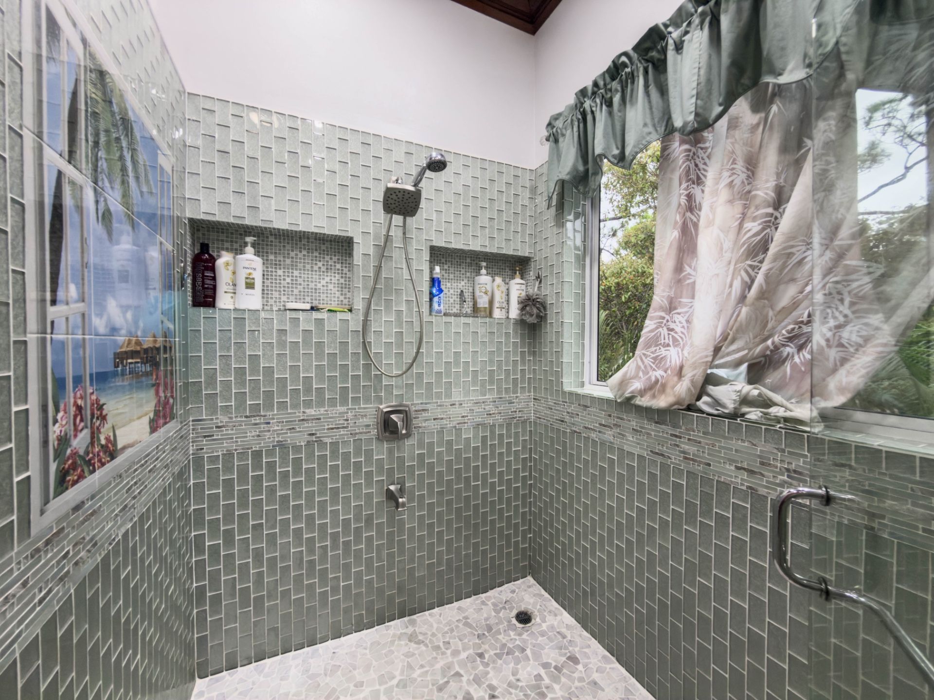 Walk-in shower with green glass tile, handheld showerhead and window with pebble floor