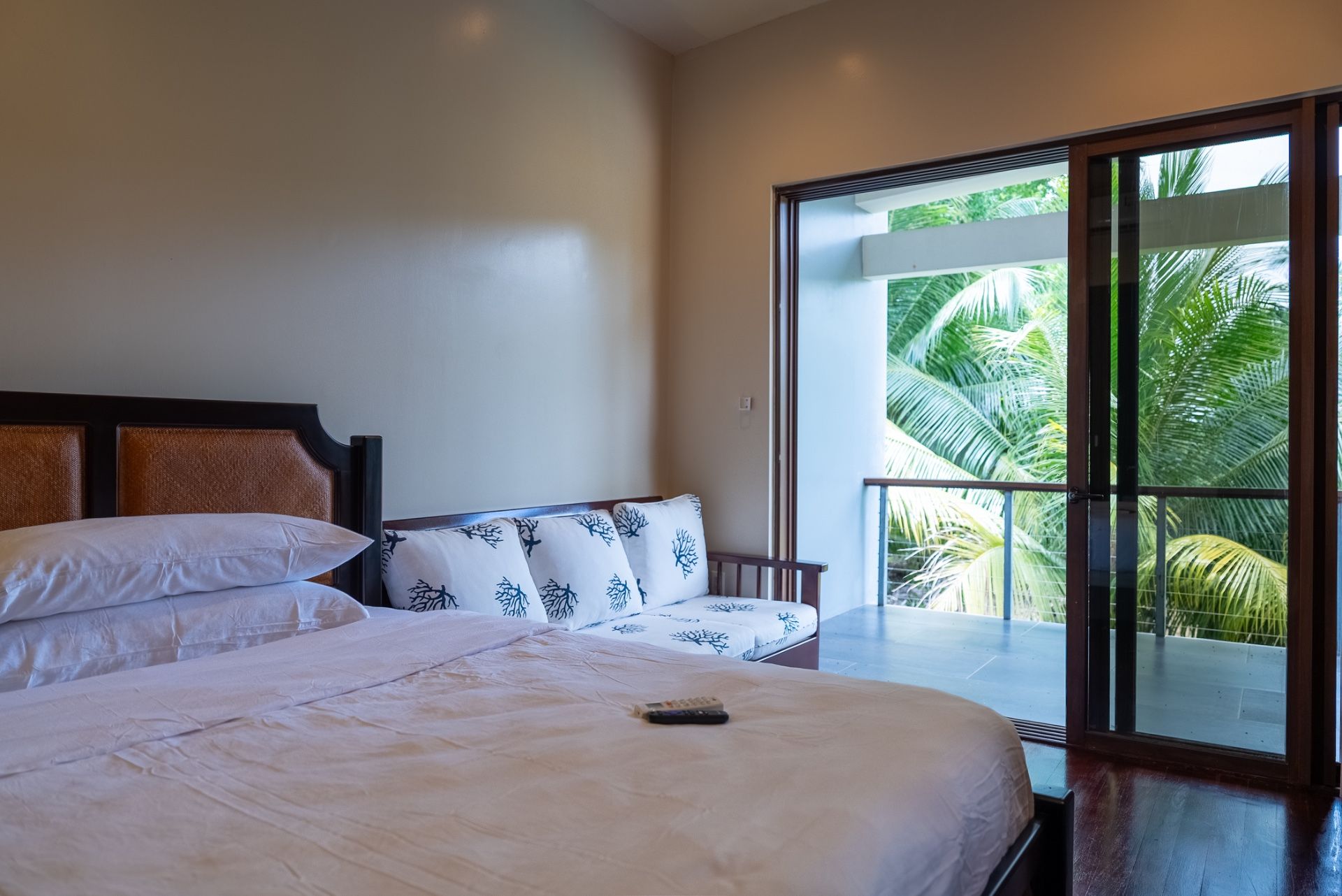Bedroom with daybed of white coral-print cushions beside a doorway to palm-filled balcony