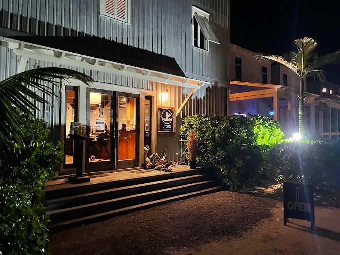 Evening view of a lit storefront entrance with glass doors, steps and palm plants
