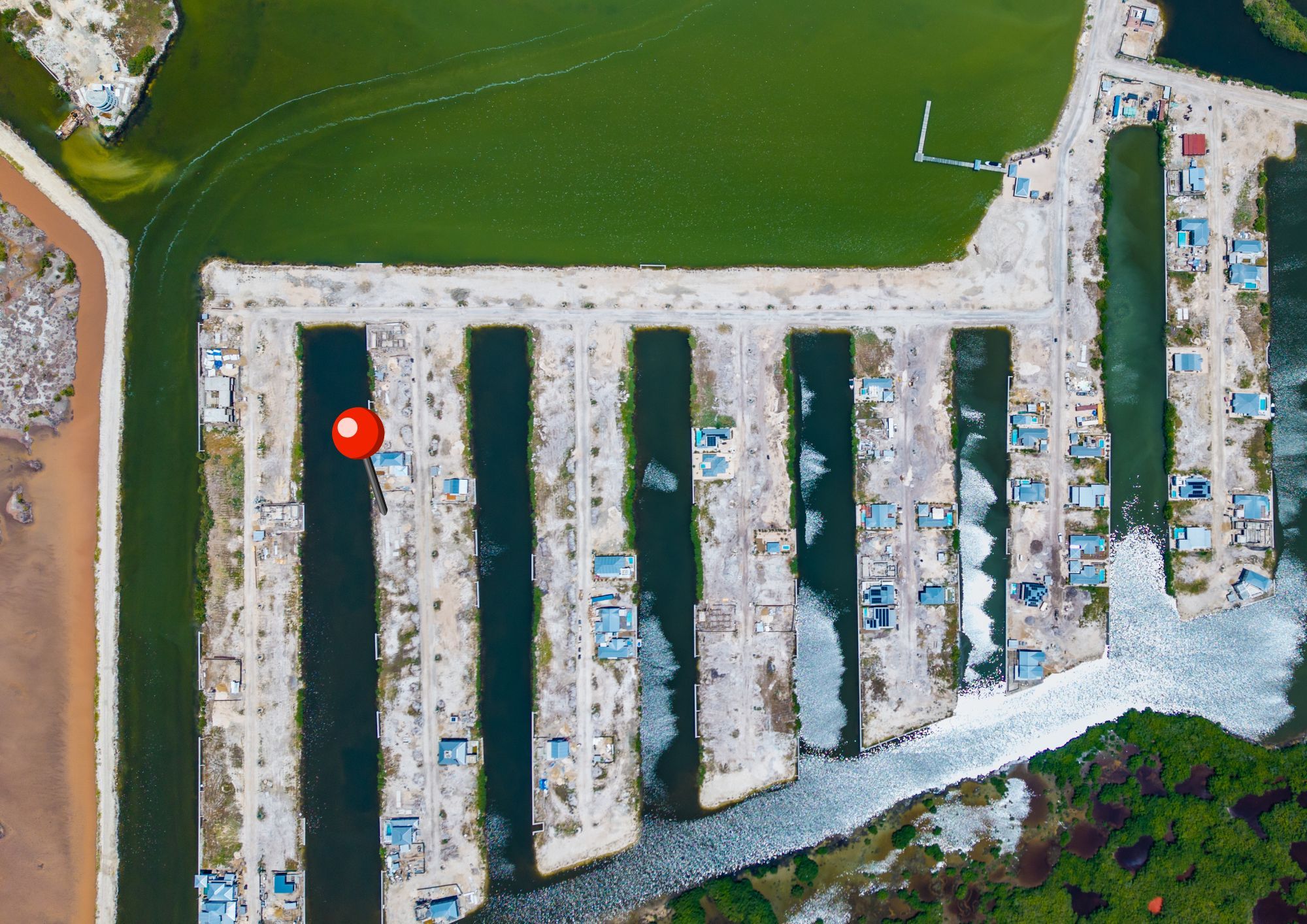 Aerial view of canal-side lots with small blue-roofed buildings beside green water