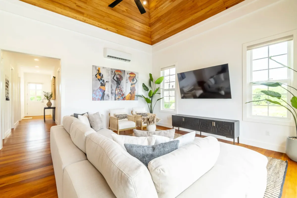 Living room with white sectional sofa, wood-paneled ceiling and three framed figure paintings
