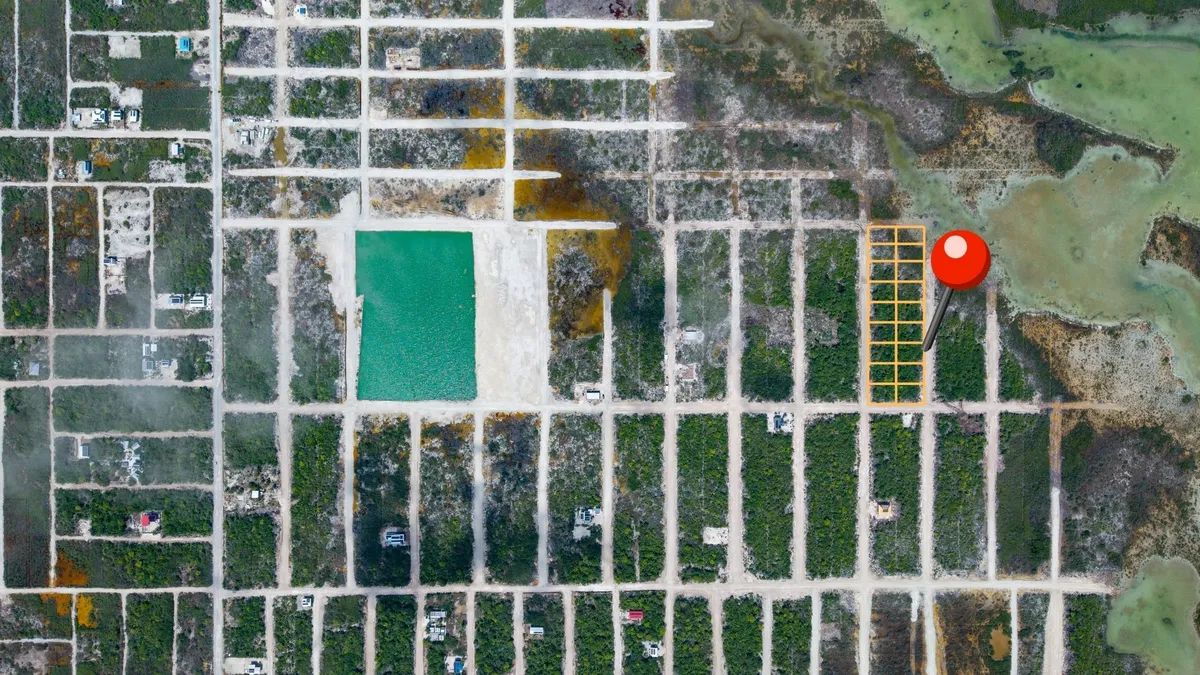 Aerial view of subdivided land lots with dirt roads, scrub vegetation and a turquoise pond