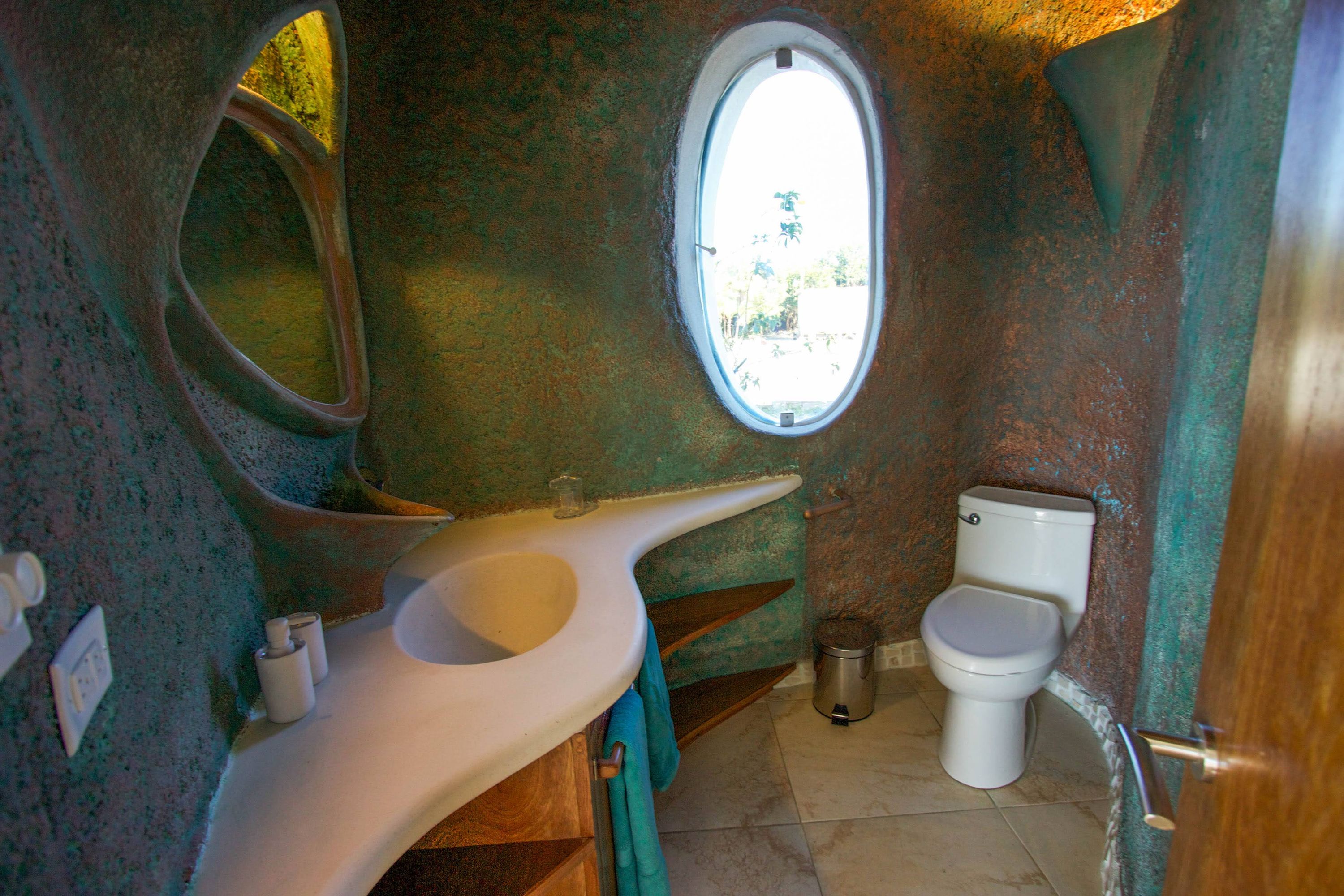Bathroom with mottled green wall, oval window and white sculpted vanity