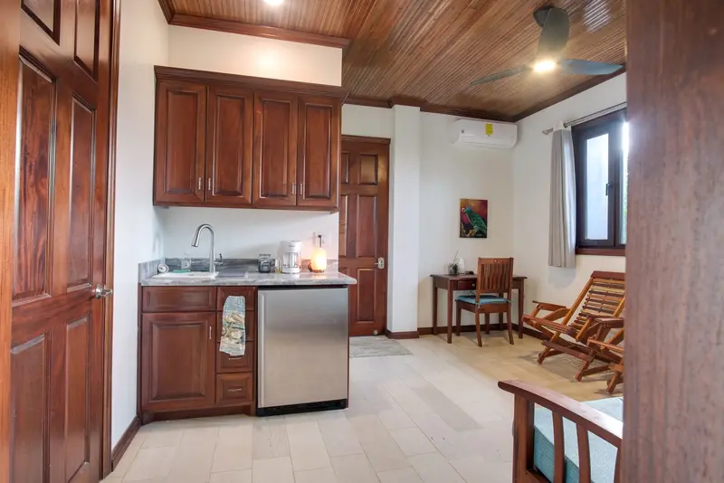 Compact kitchenette with wood cabinets, steel mini fridge and small writing desk