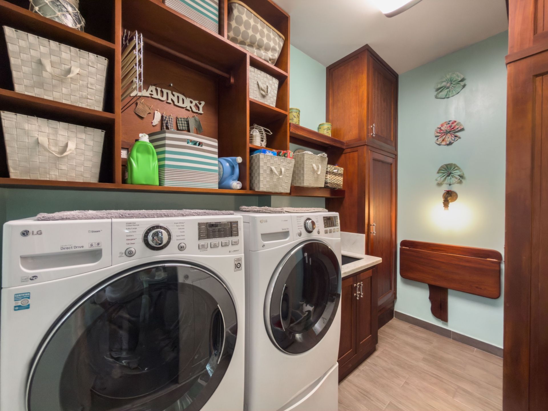 Laundry room with front-load washer and dryer beneath wooden open shelving with baskets