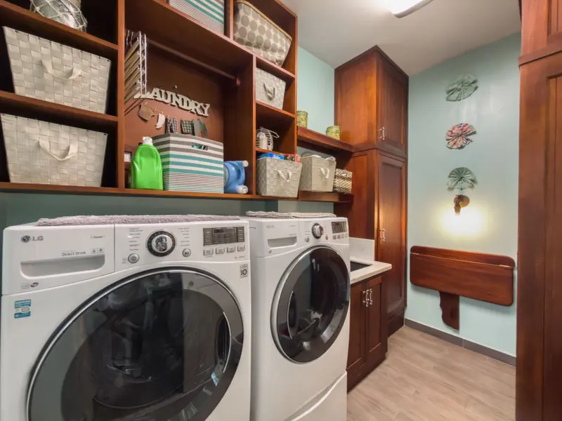 Laundry room with front-load washer and dryer beneath wooden open shelving with baskets