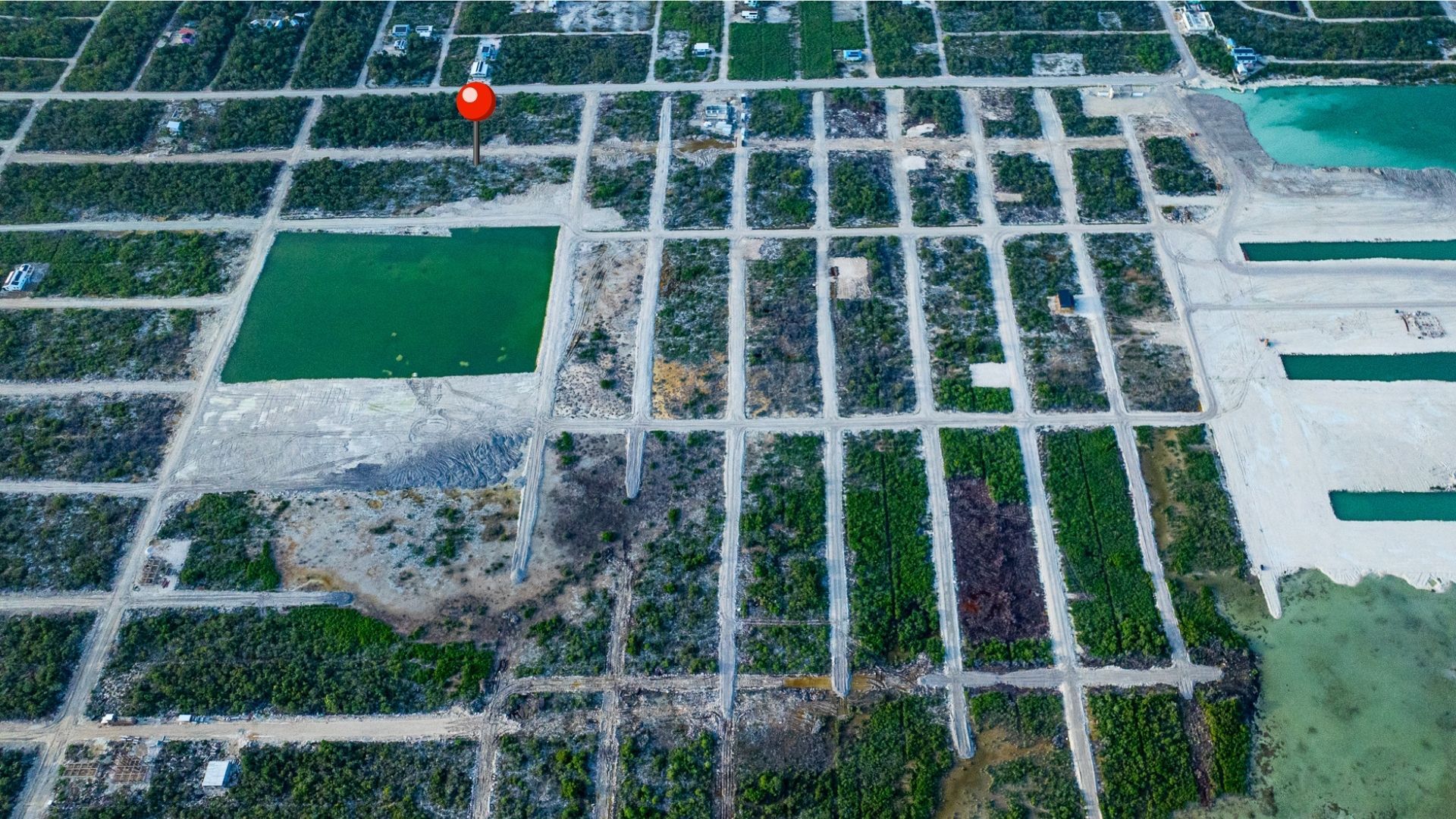 Aerial view of gridded residential lots with dirt roads and green water pond