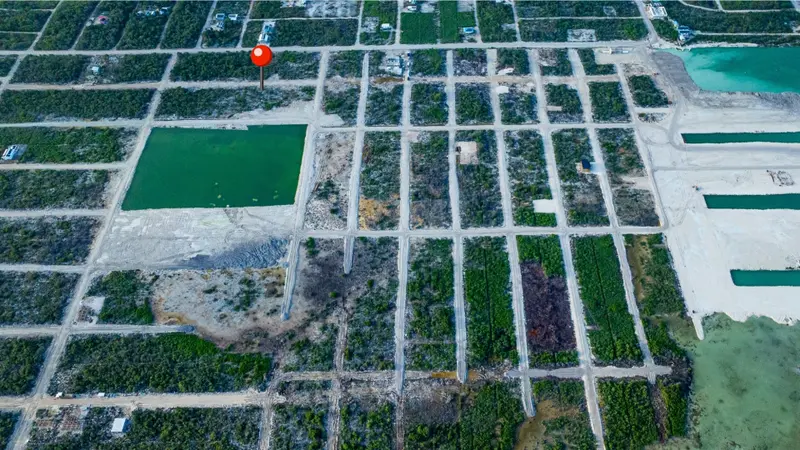Aerial view of gridded residential lots with dirt roads and green water pond