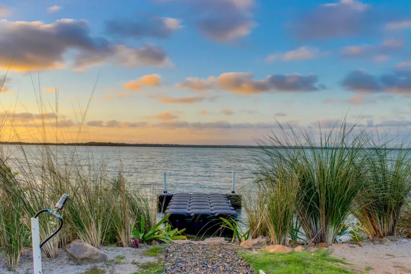 Floating dock on calm water at sunset with grasses along the shore