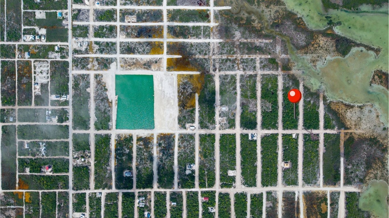Aerial view of gridded land lots with dirt roads and a turquoise pool-like pit
