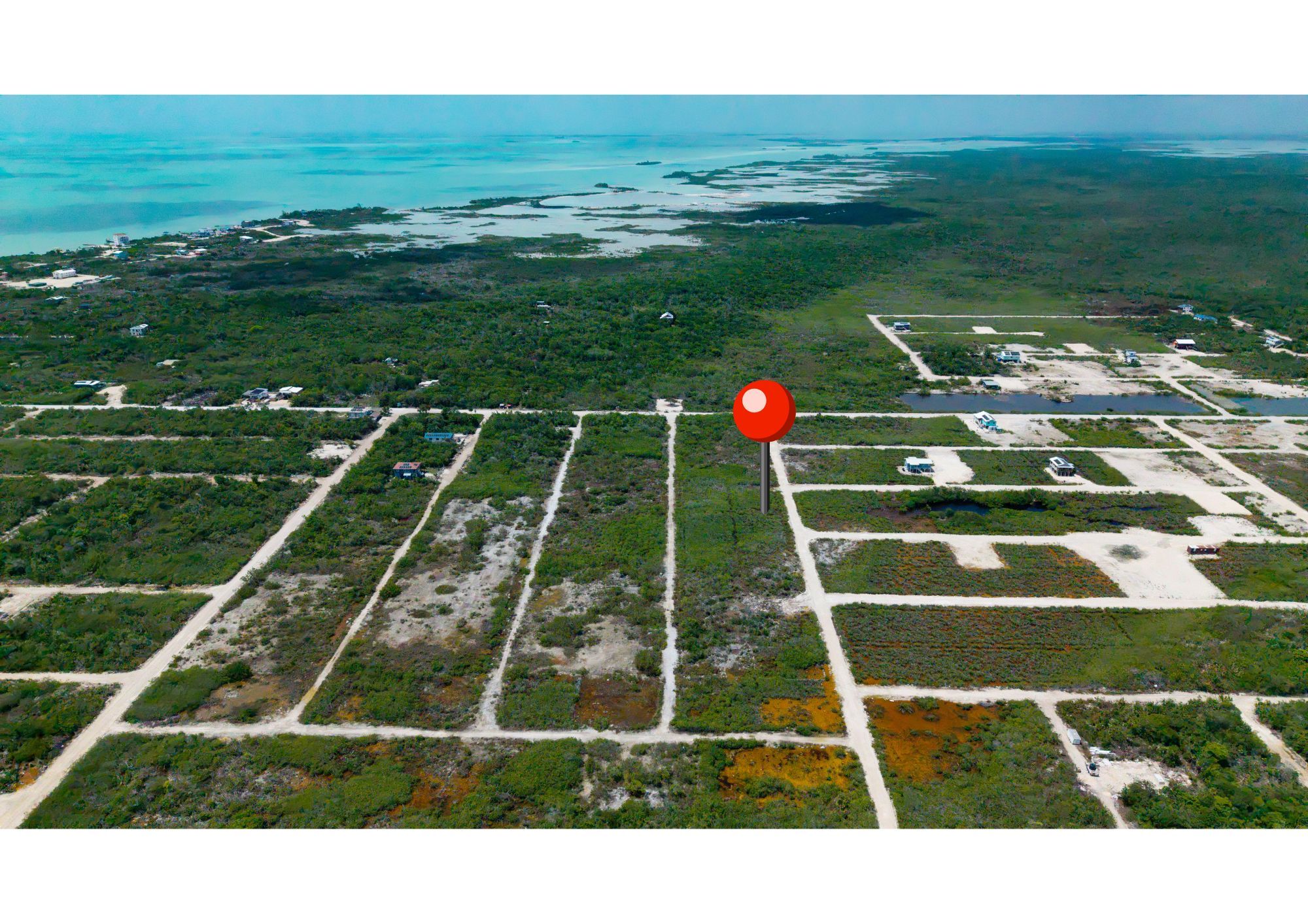 Aerial view of subdivided land lots with dirt roads and a red location pin