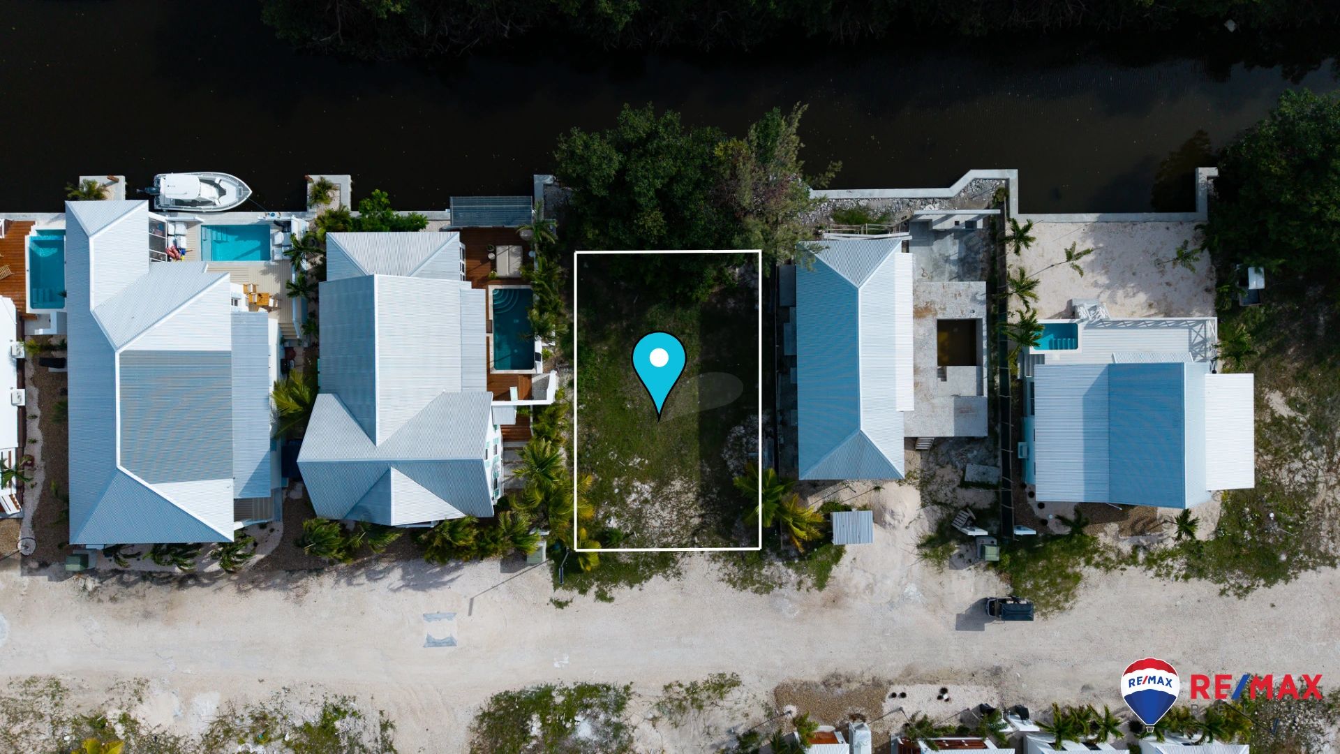 Aerial view of a vacant lot outlined in white, with neighboring houses and a pool