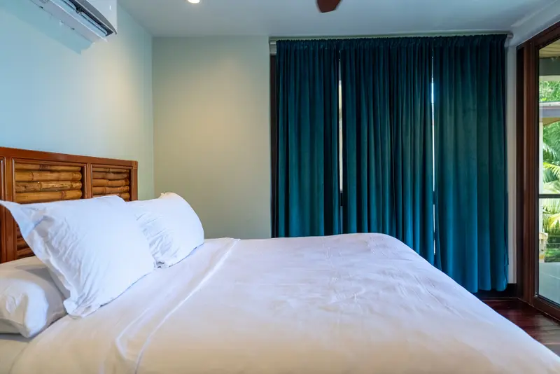Bedroom with white bed linens and teal velvet curtains at window