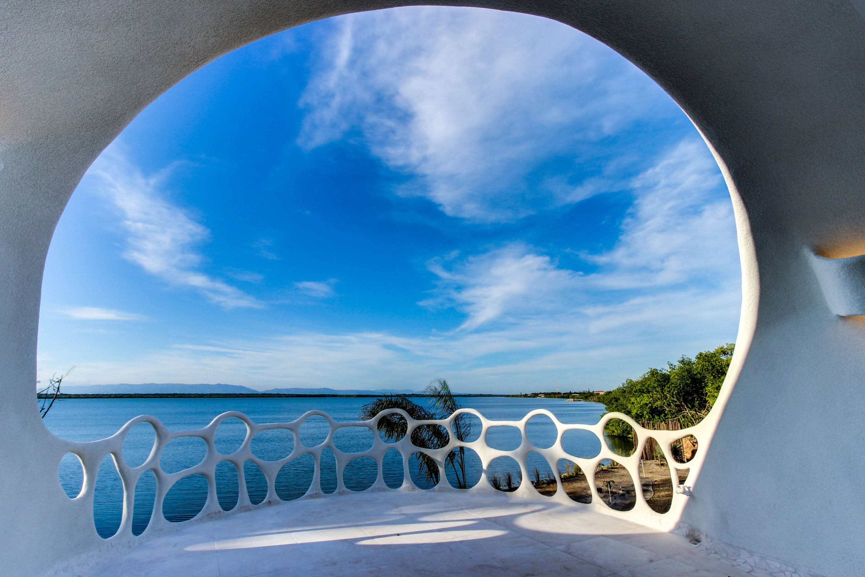 Terrace with white sculptural openwork railing overlooking calm water and palm fronds