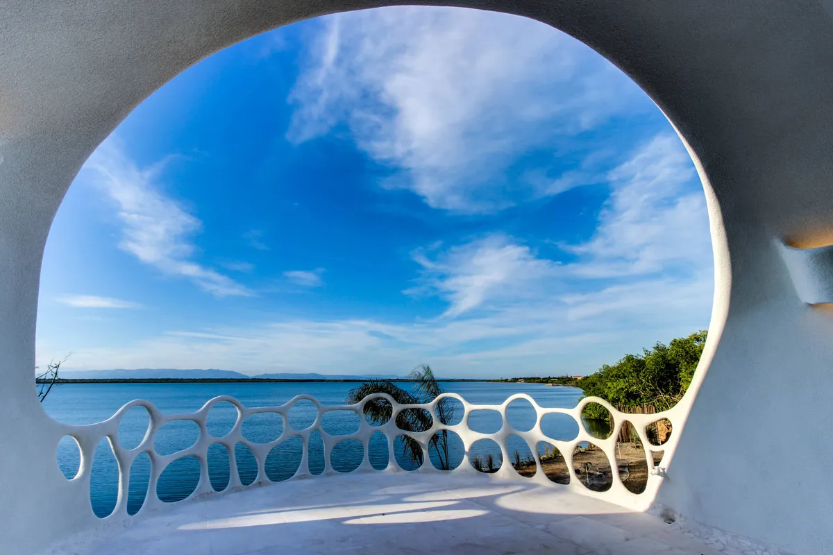 Terrace with white sculptural openwork railing overlooking calm water and palm fronds