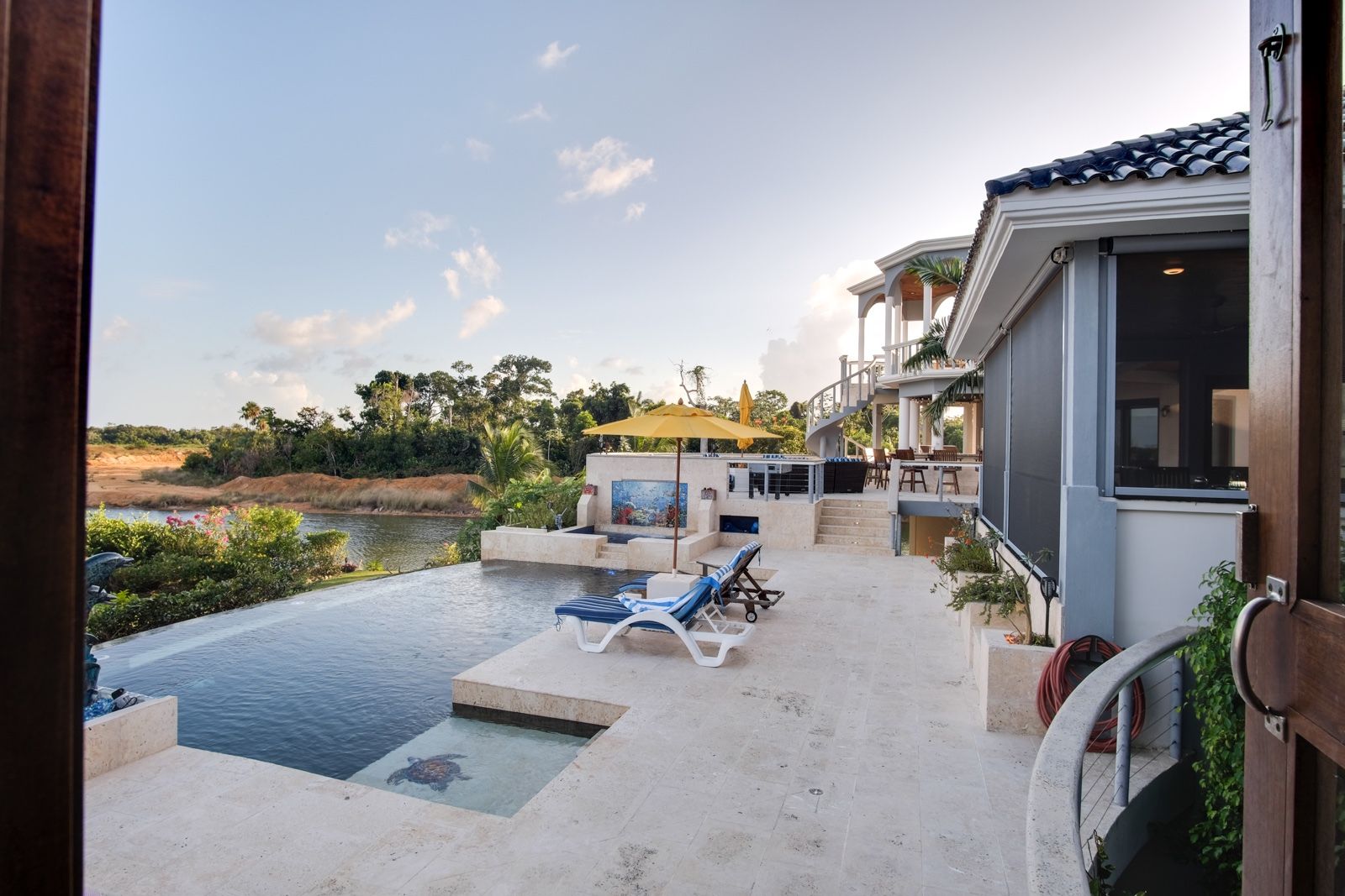 Infinity pool with turtle mosaic, loungers and yellow umbrella beside villa terrace