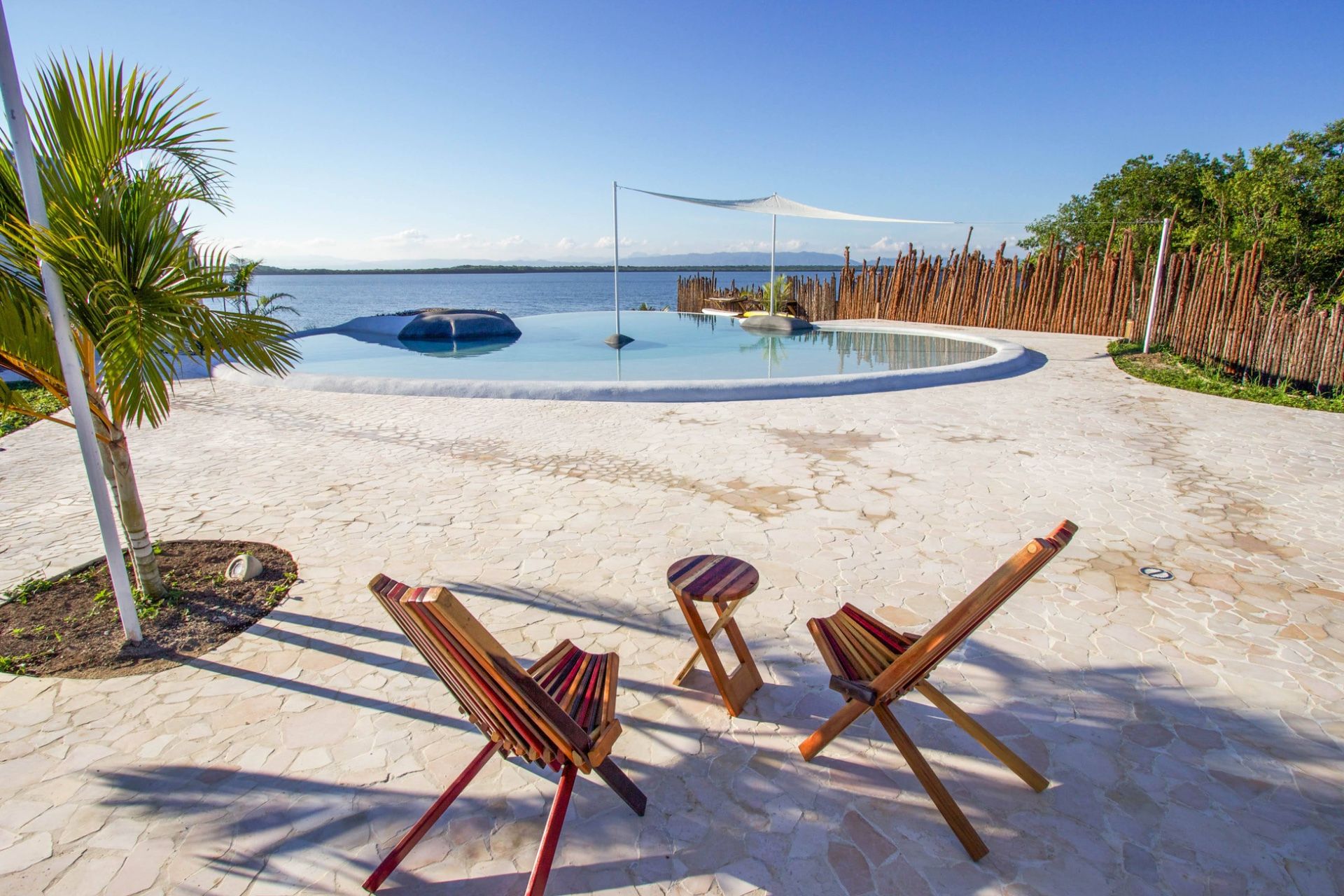Infinity pool with wooden lounge chairs on stone patio overlooking water