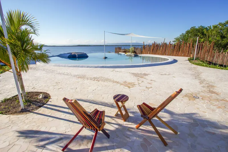 Infinity pool with wooden lounge chairs on stone patio overlooking water