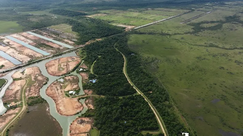 Aerial view of cleared land lots beside a winding canal and dense green trees