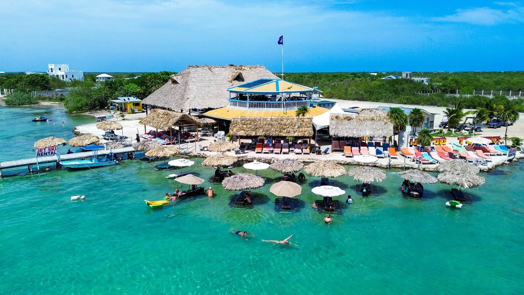 Aerial view of thatched beach bar above turquoise water with swimmers and umbrellas