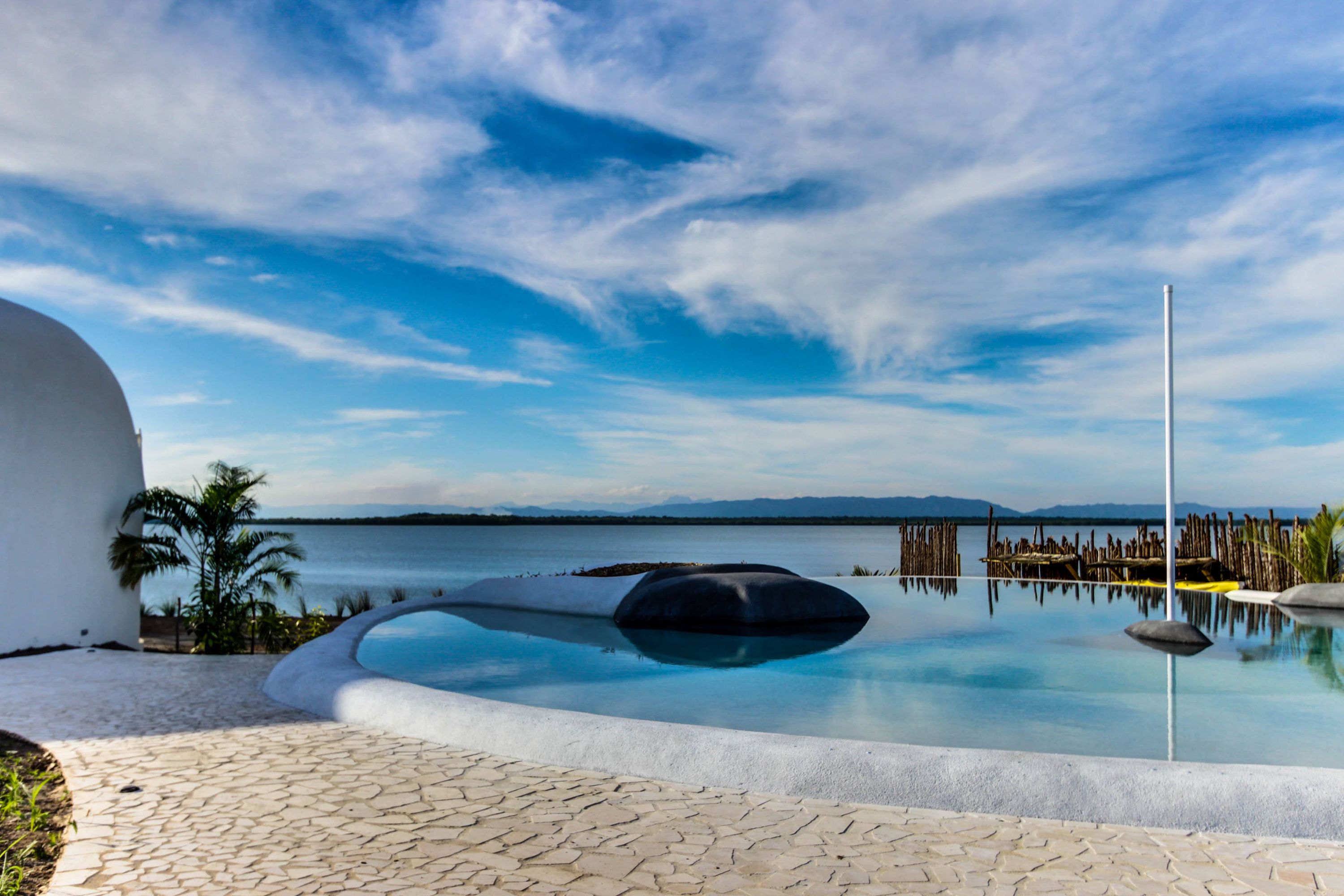 Pool edge with dark rounded stone sculpture over calm water and mountains beyond