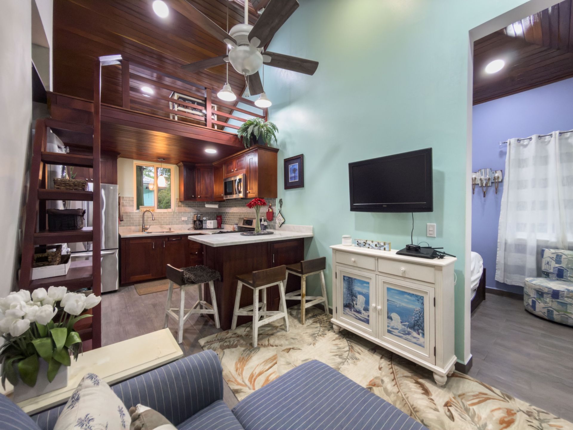 Small kitchen with dark wood cabinets and bar stools beside a flat screen TV