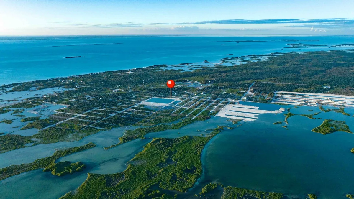 Aerial view of coastal lots with a red location pin over green mangrove land and blue water
