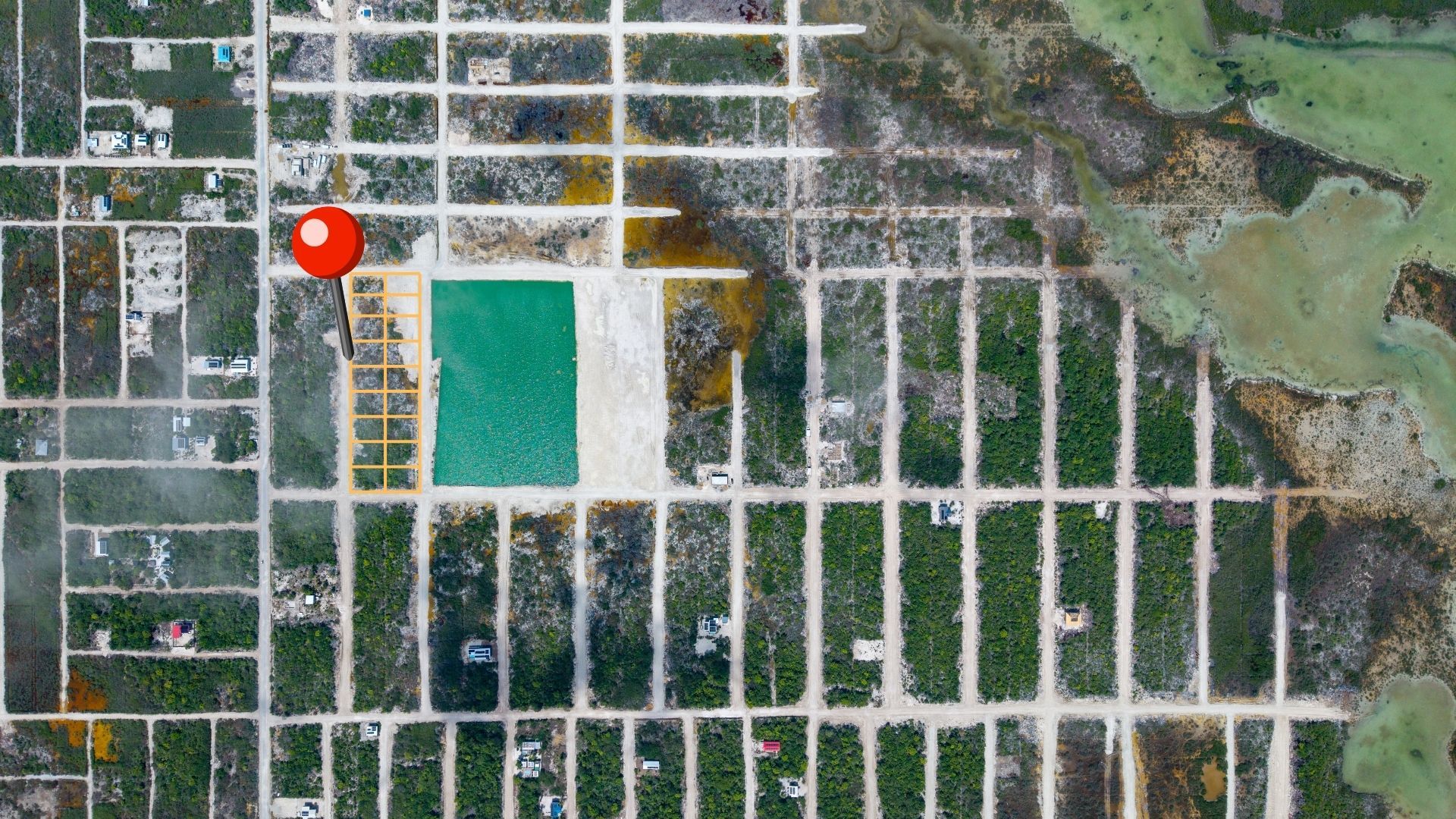 Aerial view of subdivided lots with dirt roads and a turquoise pond