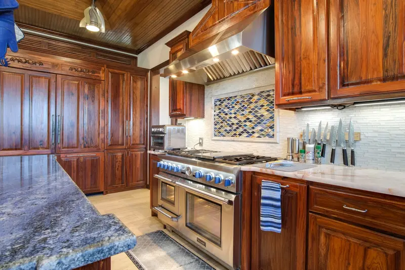 Kitchen range with blue knobs under stainless hood beside dark wood cabinets