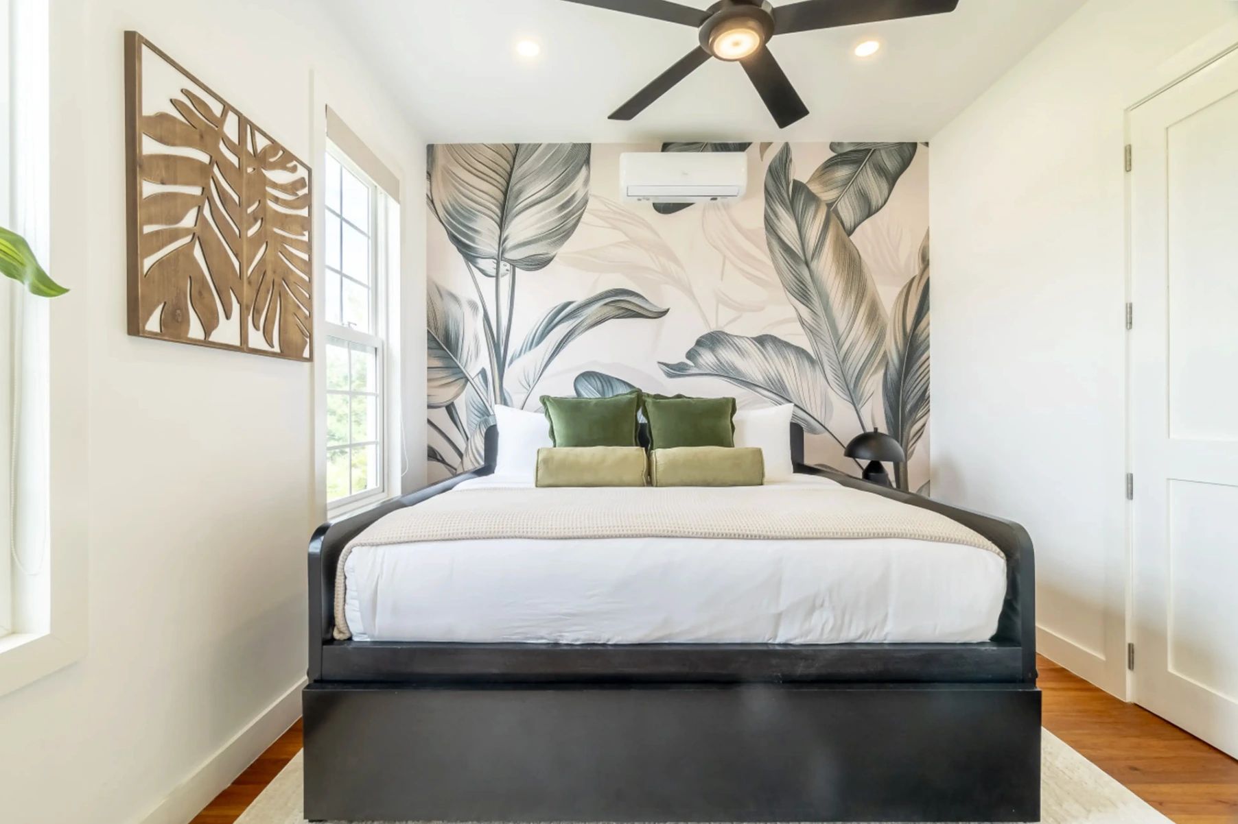 Bedroom with king bed, green velvet pillows and large leaf mural wallpaper
