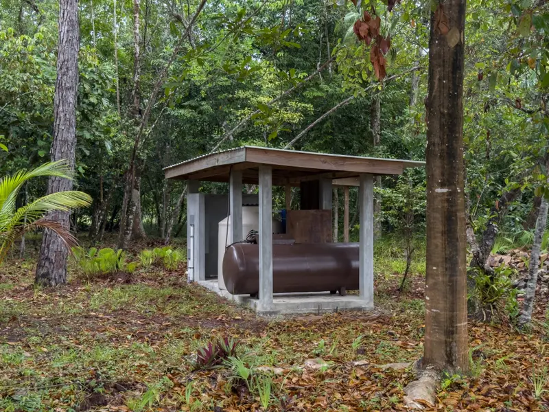 Covered utility shelter with brown tank and white water tank among forest trees