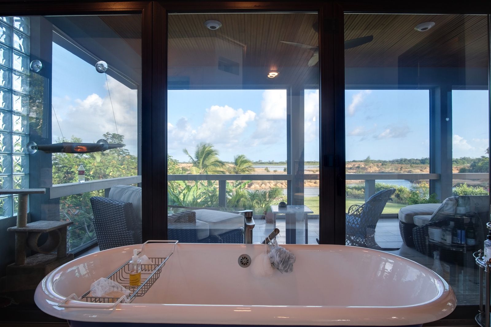 Freestanding white bathtub facing glass doors onto a palm-lined balcony