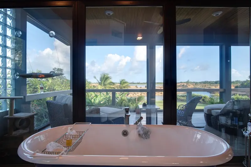 Freestanding white bathtub facing glass doors onto a palm-lined balcony