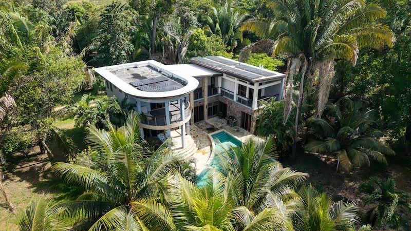 Aerial view of modern house with rooftop solar panels, pool and palm trees