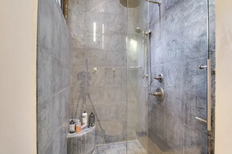 Walk-in shower with grey stone-look tiles, brushed nickel fixtures and glass enclosure