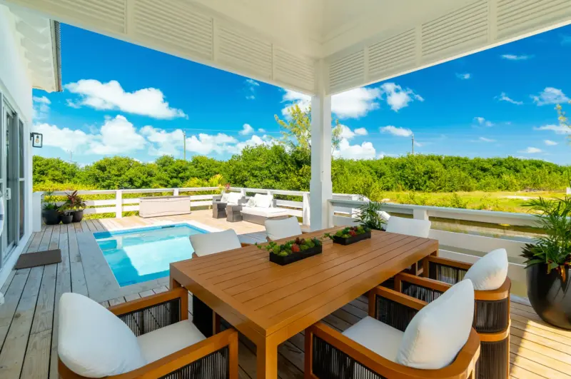 Covered outdoor dining area with wooden table, white chairs and pool beyond