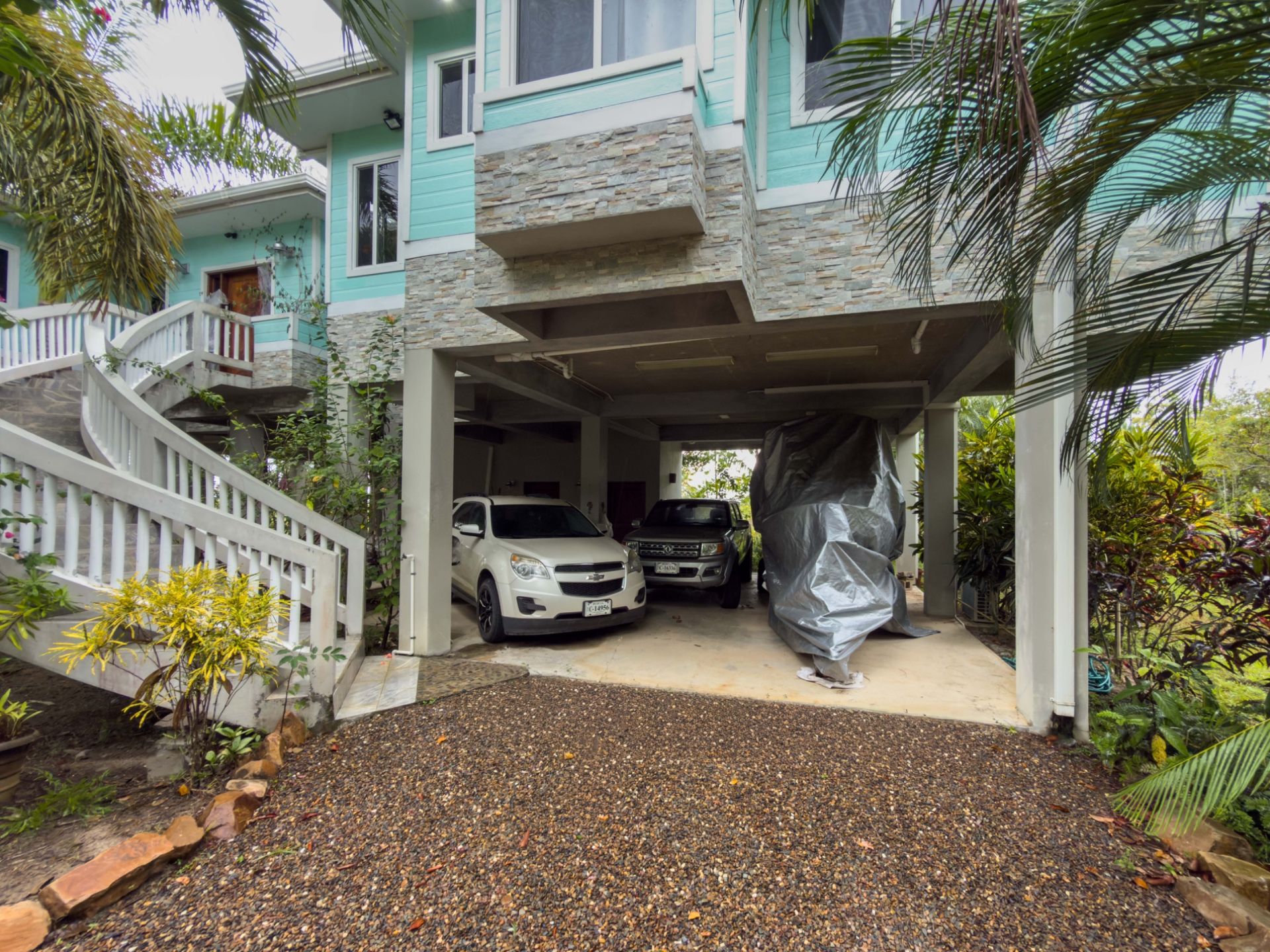 Covered carport under teal house with stone cladding and two parked cars