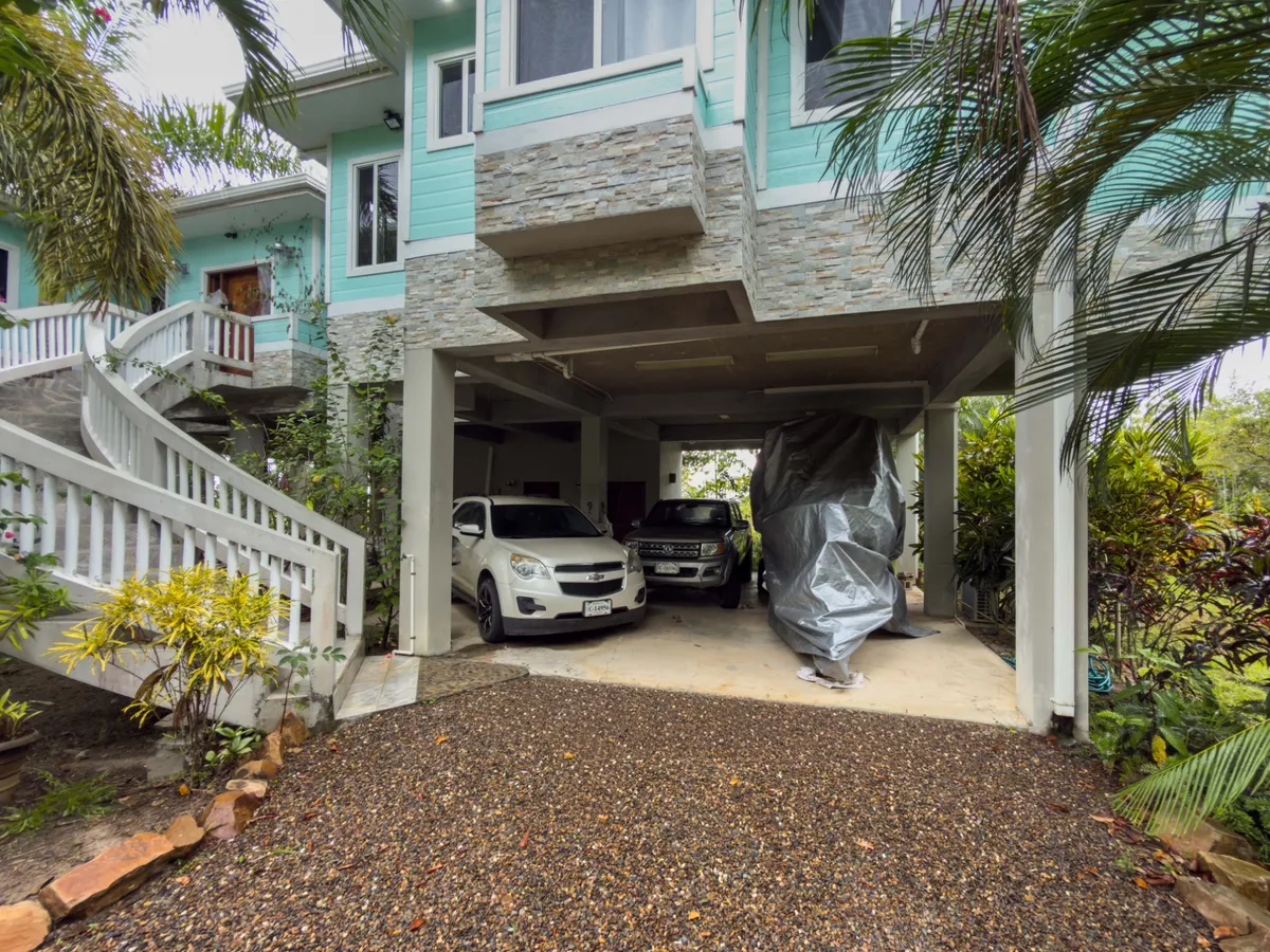 Covered carport under teal house with stone cladding and two parked cars