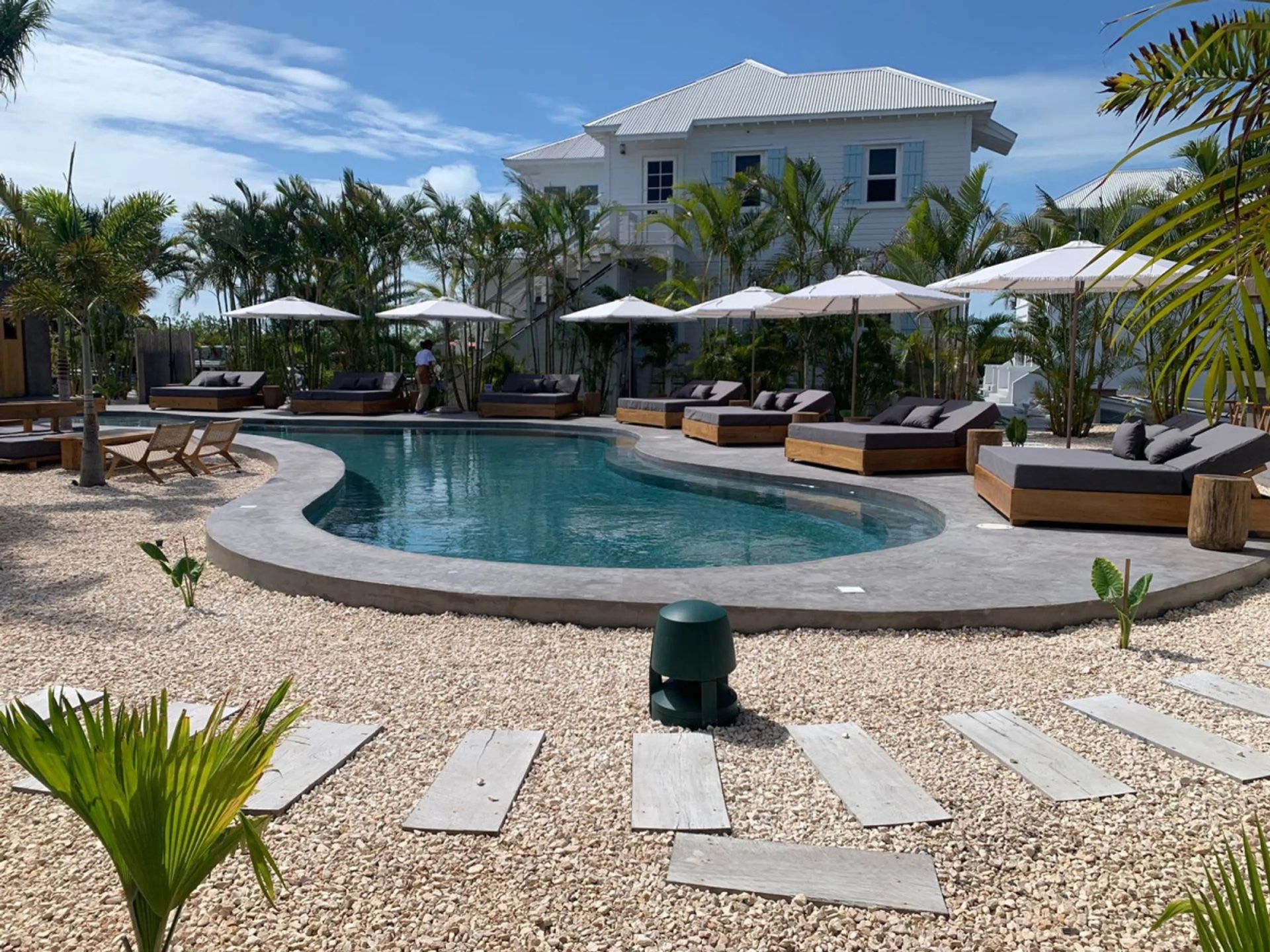 Pool with curved edge, teak loungers and white umbrellas beside a white two-storey house