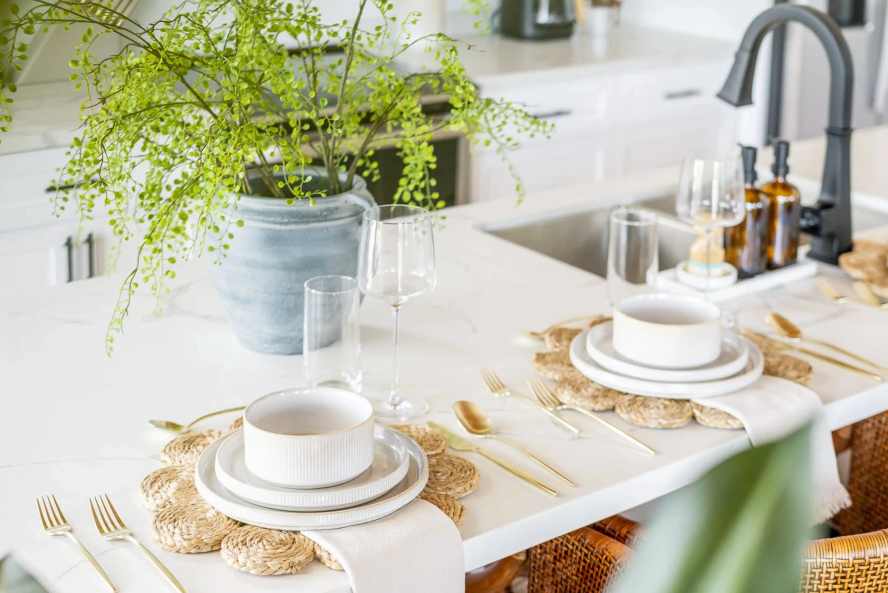 Kitchen island set with white dishes, gold cutlery and a fern in a blue vase