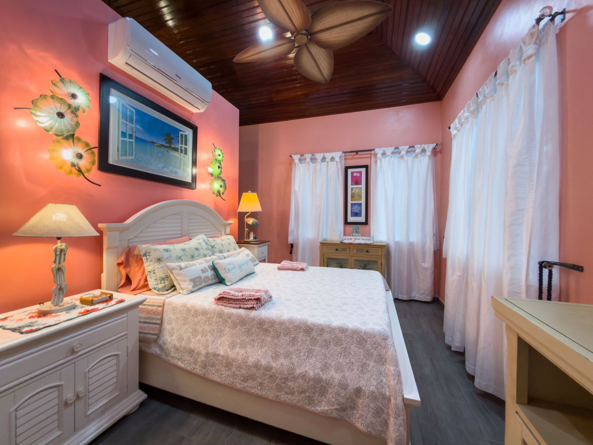 Bedroom with pink walls, white bed and wood-paneled ceiling fan