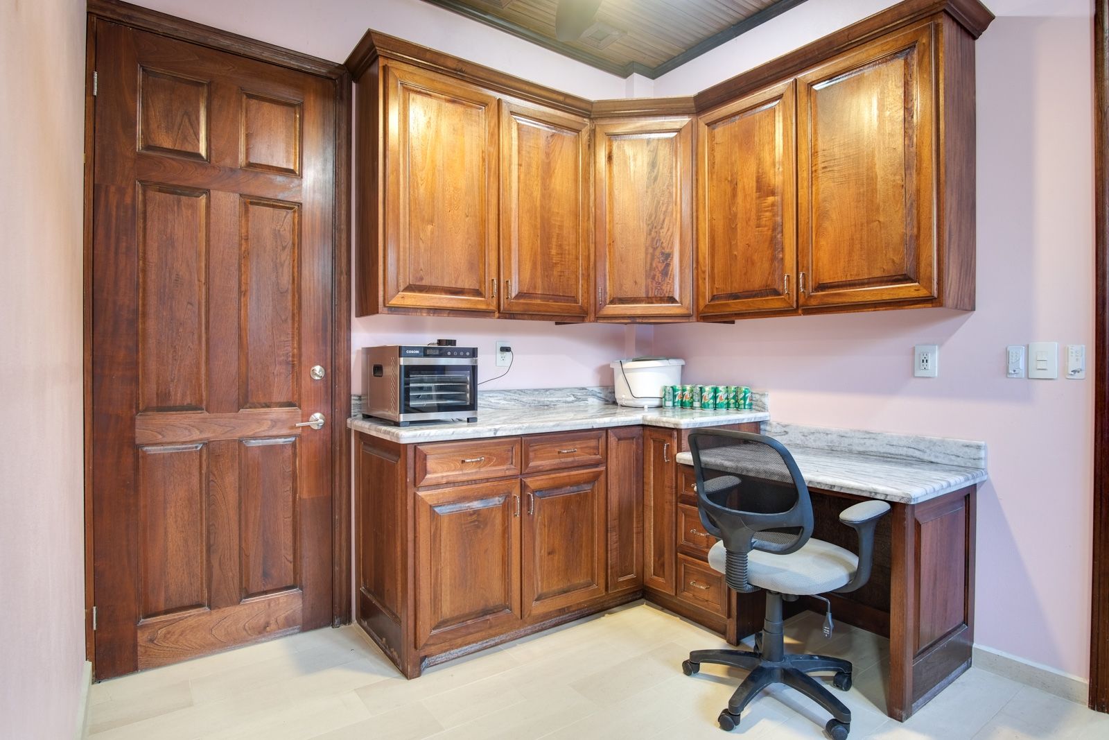 Kitchen corner with dark wood cabinets, marble counters and a rolling desk chair