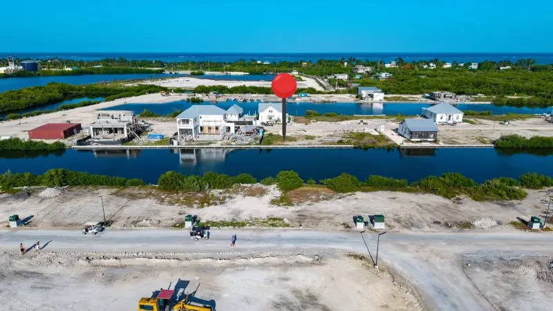 Aerial view of cleared land beside a canal with white houses across the water