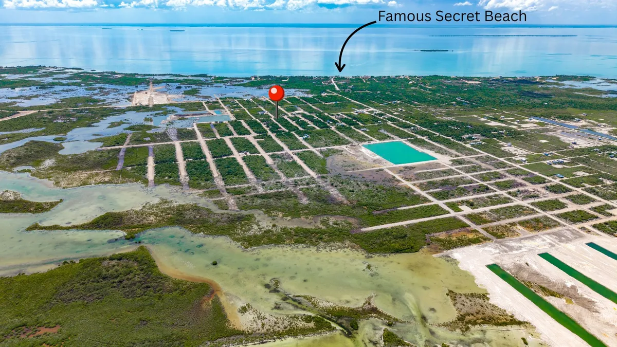 Aerial view of coastal land parcels with dirt roads, scrub vegetation and a turquoise pool-like basin