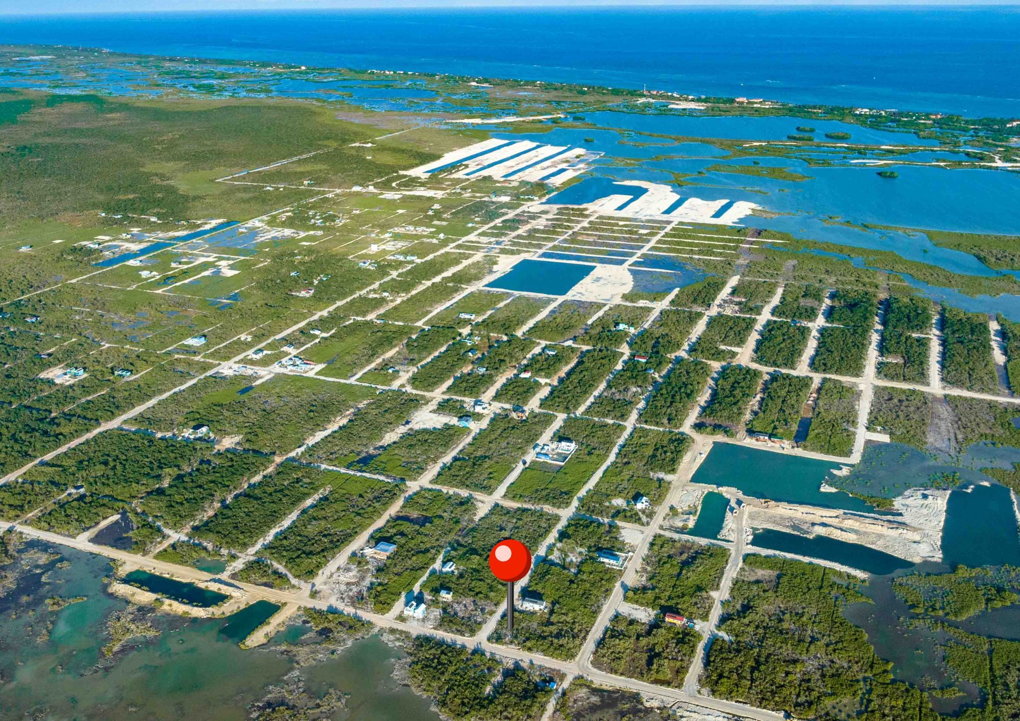 Aerial view of gridded residential lots with scattered small buildings and sea beyond