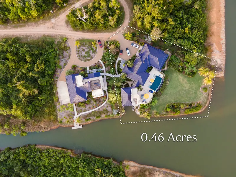 Aerial view of blue-roofed home beside pool, waterway and driveway